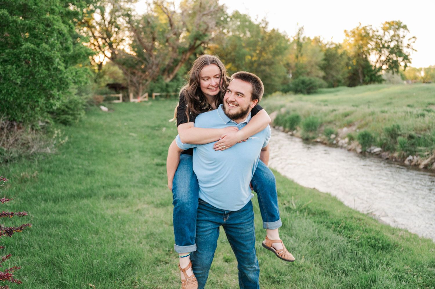 Playful piggyback ride along riverside path during sunset engagement session.