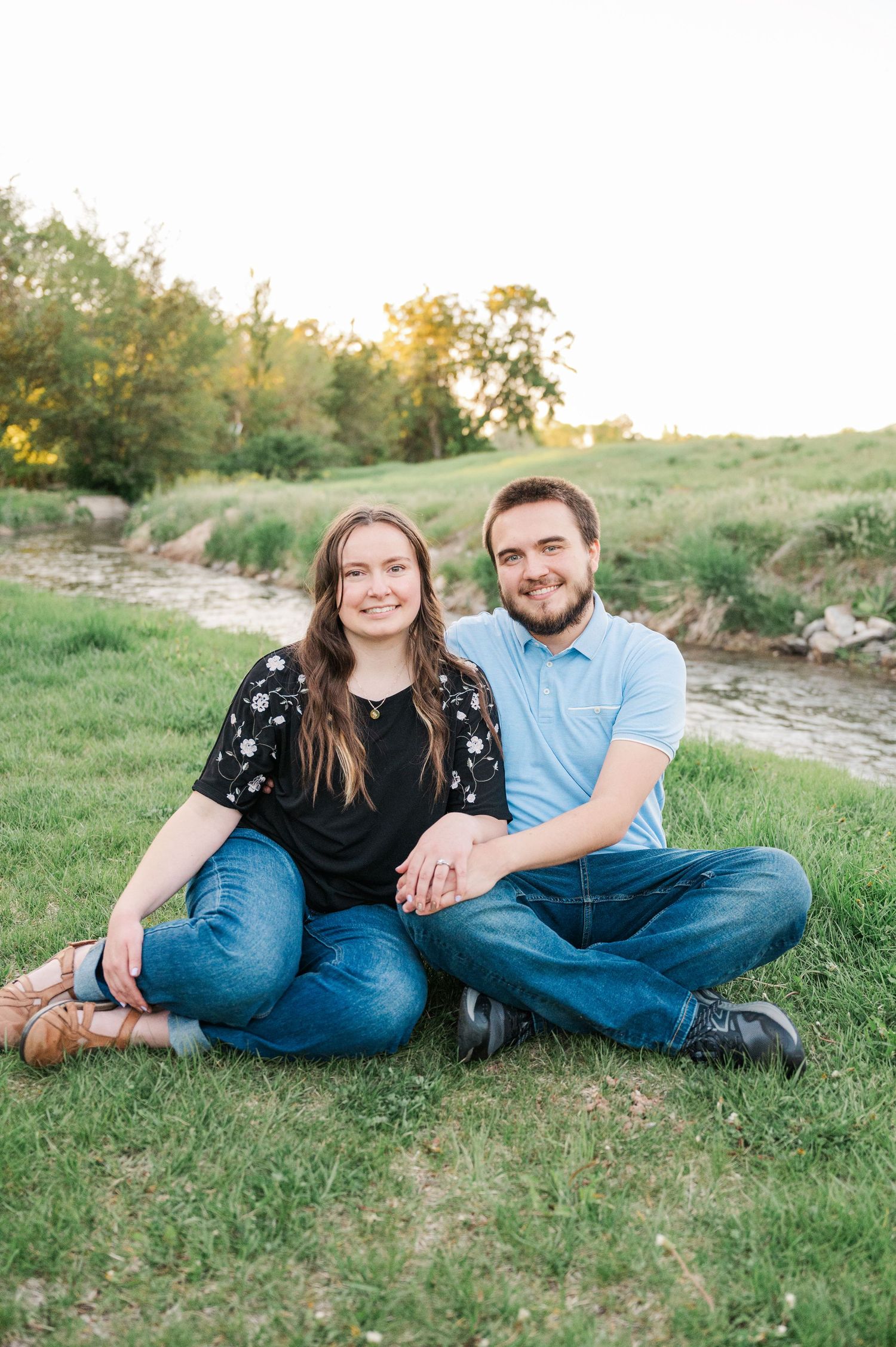 Casual couple sitting together on grassy riverbank at sunset.