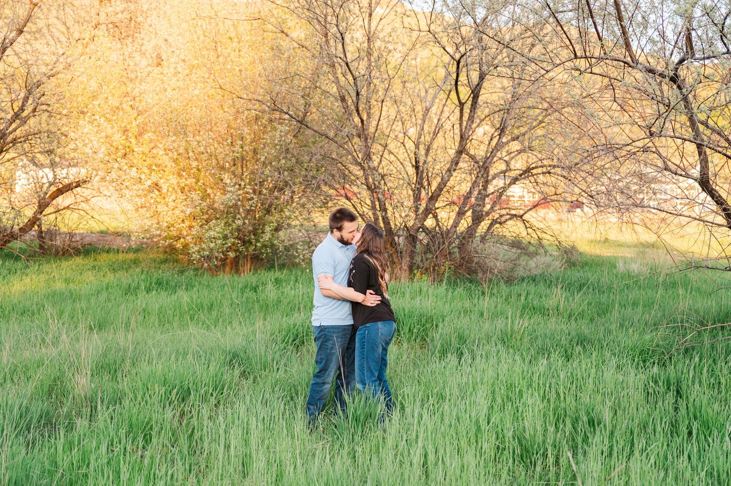 A couple shares an intimate moment while standing in tall grass at golden hour.