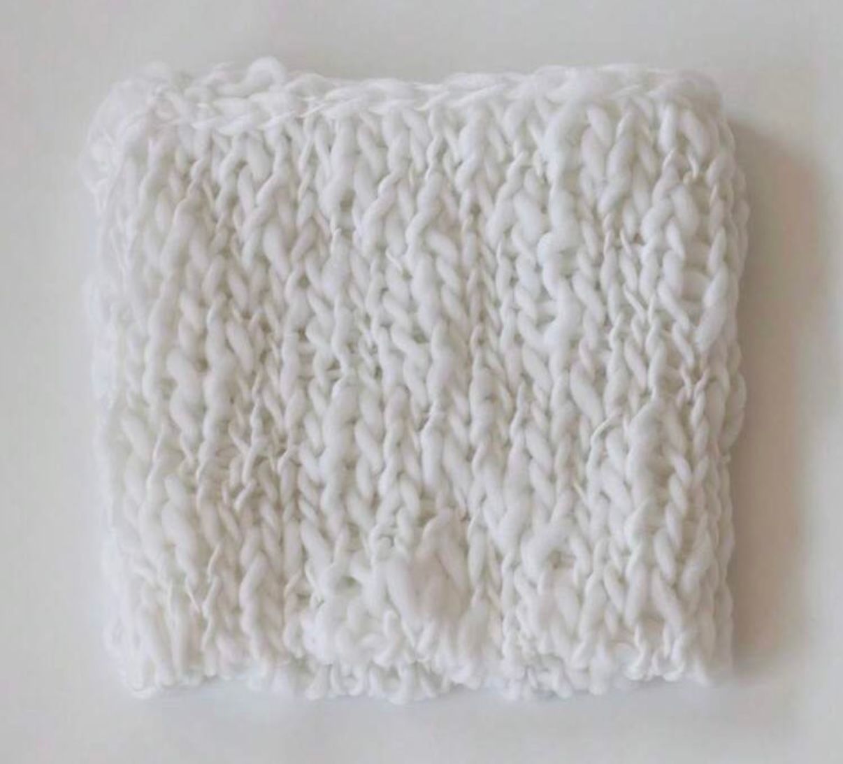 Close-up of white chunky knit wool texture pattern against light background.