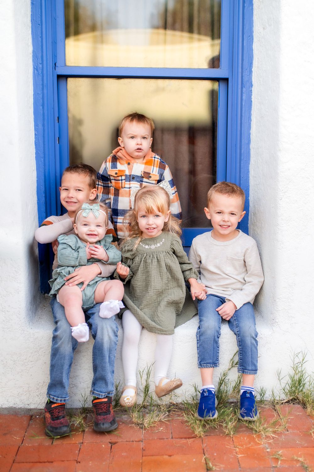 Five young children sitting and smiling together in a blue-framed window alcove.