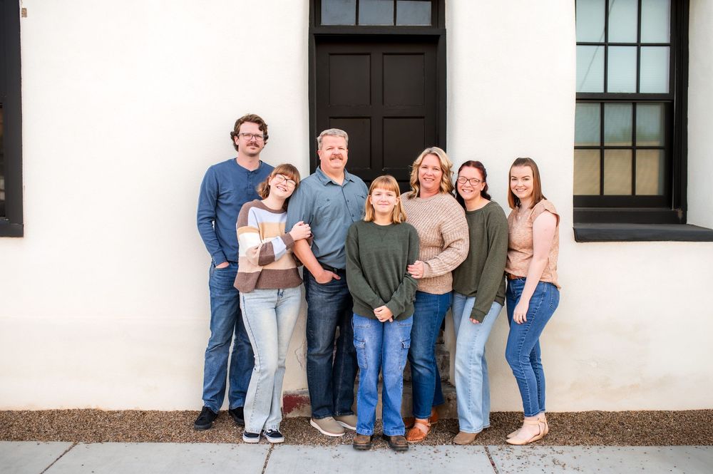 Happy family of seven posing together outside a building with a black door.