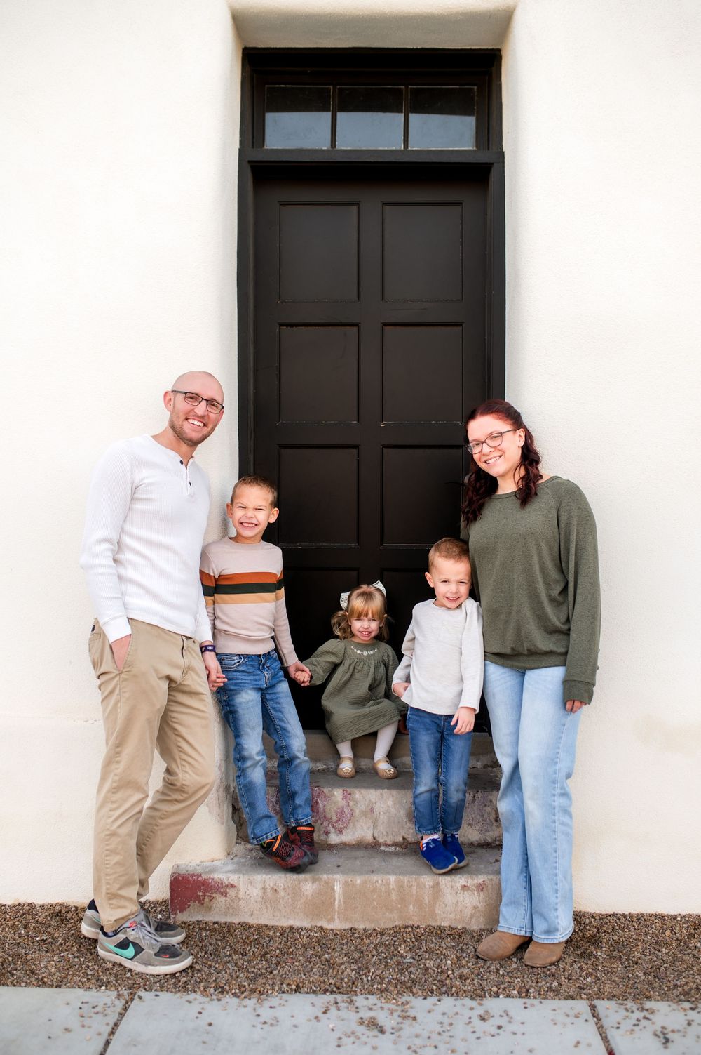 Family of five smiling together on steps in front of a black door.