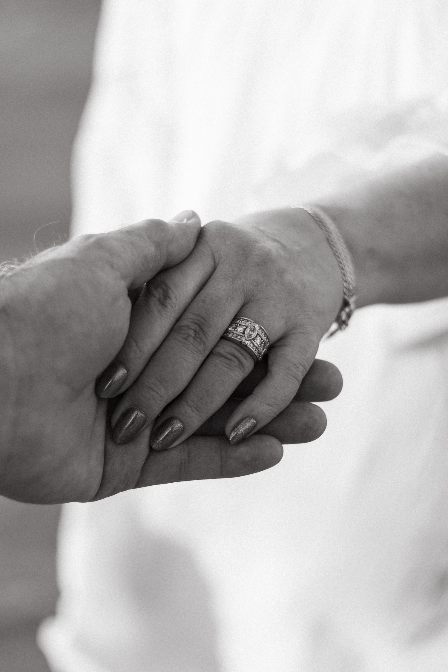 Close up black and white photo of hands holding with wedding ring visible.