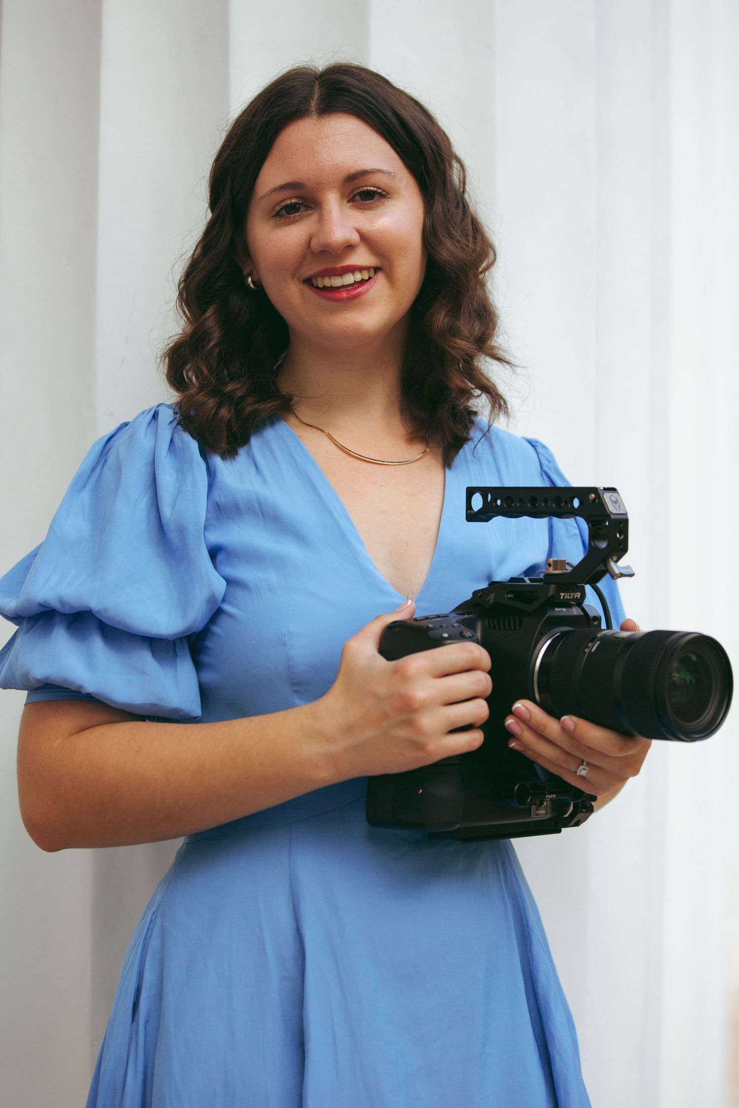 Professional photographer in blue dress holding DSLR camera with mounted equipment.