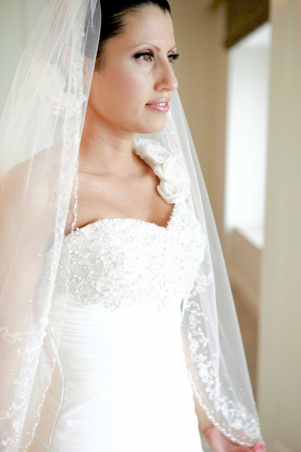 A bride wearing a white beaded wedding dress and traditional veil gazes to the side.