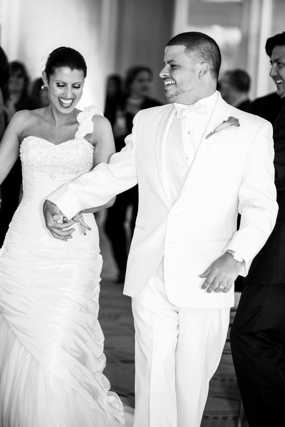 A joyful couple dances together at their wedding reception, with the bride in white gown and groom in white tuxedo.