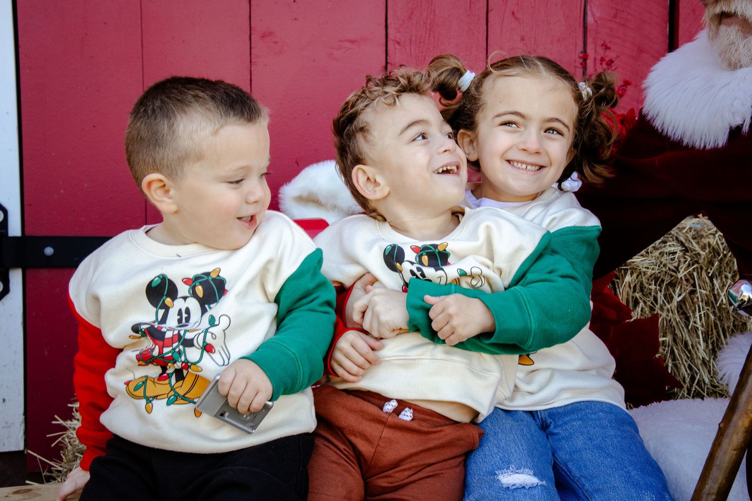 Holiday portrait session with children in festive outfits against red backdrop.