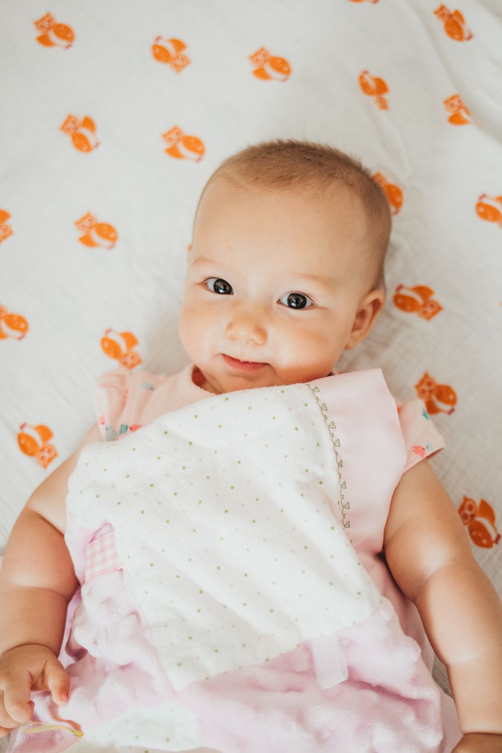A baby lying on fabric with orange fox print smiling at the camera.