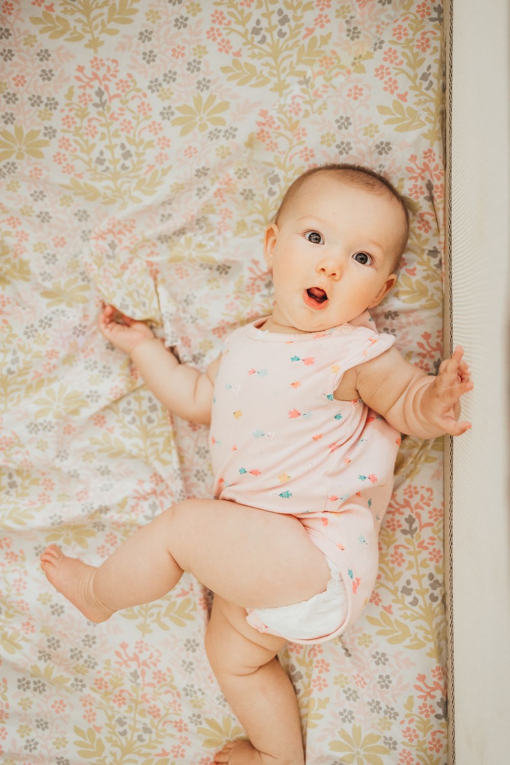 Baby in pink heart-patterned onesie lying on floral print background.