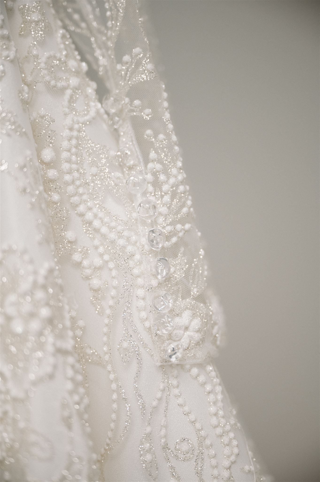 Close-up detail of intricate beaded lace and pearl embellishments on a white wedding dress.