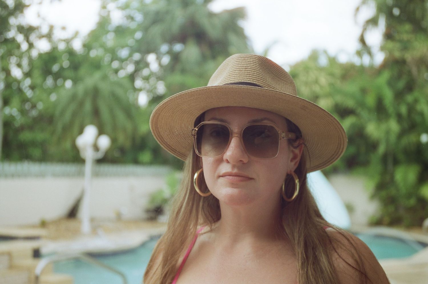 A summer poolside scene with a person wearing a straw hat and sunglasses.