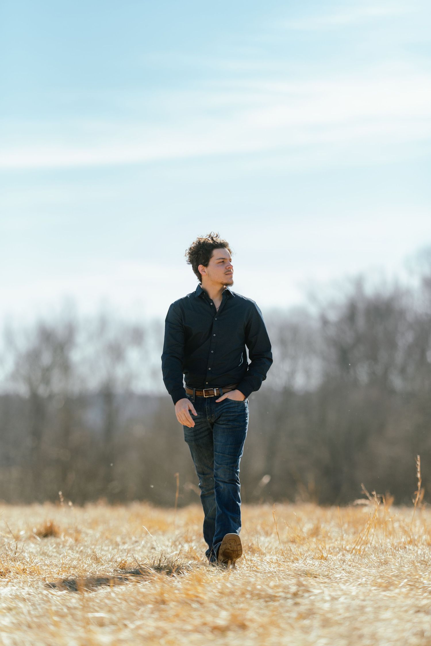 Person in dark shirt walks through golden winter field under bright sky.