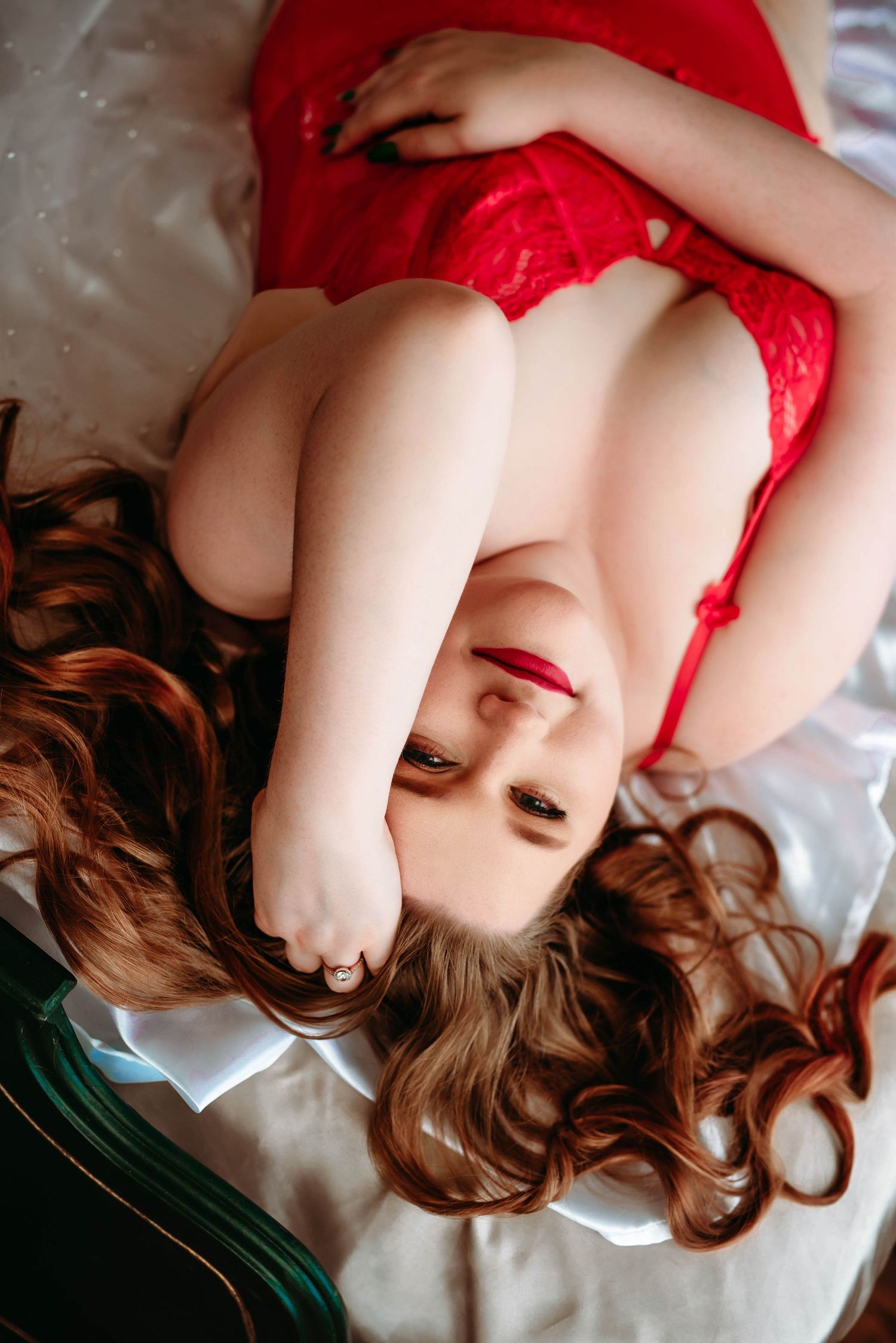 Person with wavy hair wearing red clothing lying down on light colored bedding.