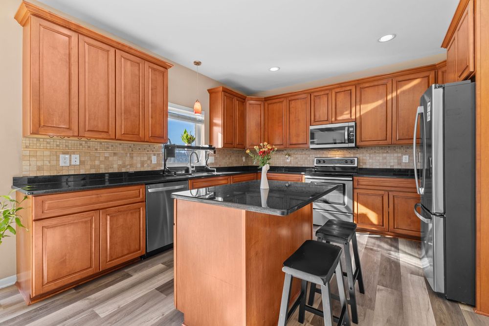 Modern kitchen with cherry wood cabinets, dark granite island, stainless steel appliances, and hardwood floors.