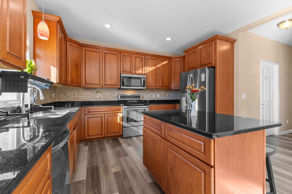 Elegant kitchen featuring cherry cabinets, dark granite countertops, stainless appliances, and hardwood flooring.