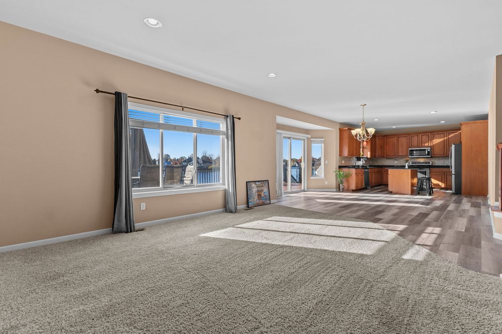 Open-concept living area with carpet flooring, large windows, and view into kitchen with stainless appliances.