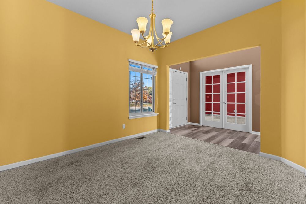 Dining room with yellow walls, chandelier, carpet flooring, and French doors leading to adjacent room.