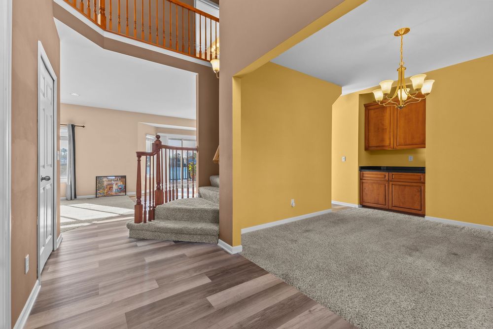 Open foyer with hardwood floors, carpeted stairs, chandelier, and built-in cabinetry in adjacent room.