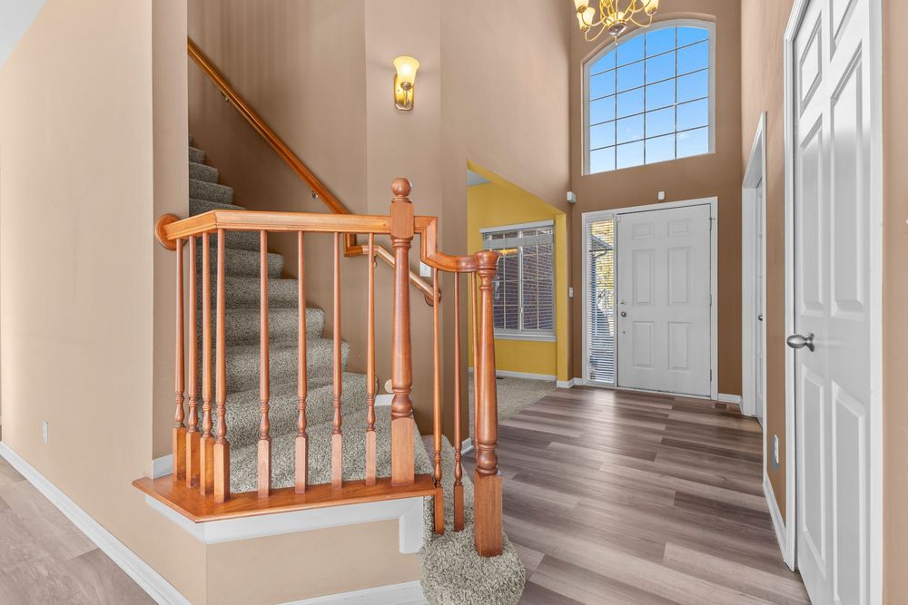 Two-story entryway with wood staircase, hardwood floors, transom window, and soaring ceiling height.