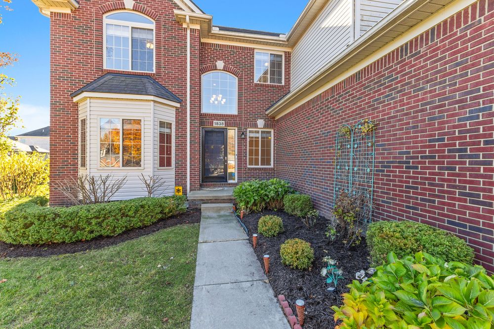 Brick two-story home exterior with manicured landscaping, arched entryway, and bay window at dusk.