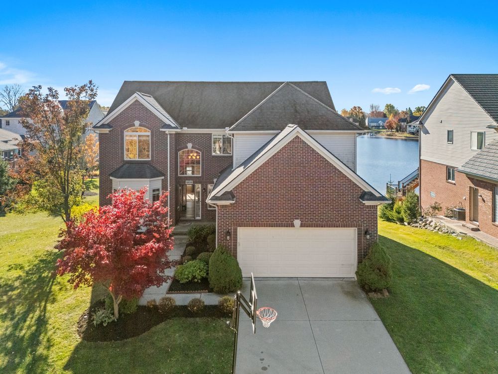 Brick two-story home with attached garage, red Japanese maple tree, and manicured lawn on a sunny day.
