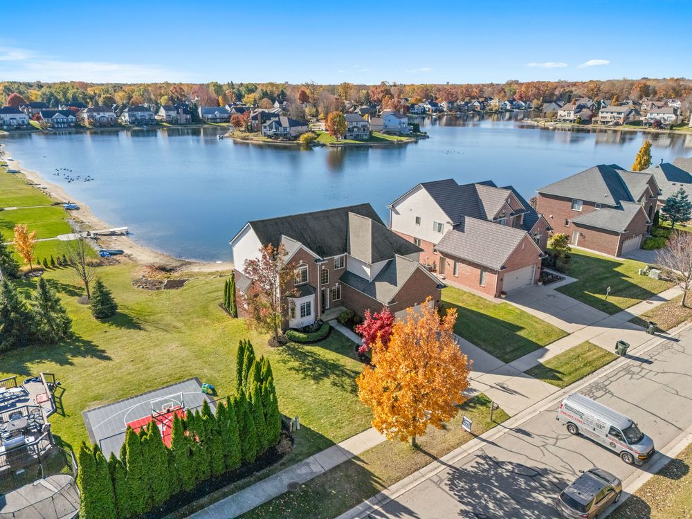 Aerial view of brick lakefront home with large yard, mature trees, and stunning water views.