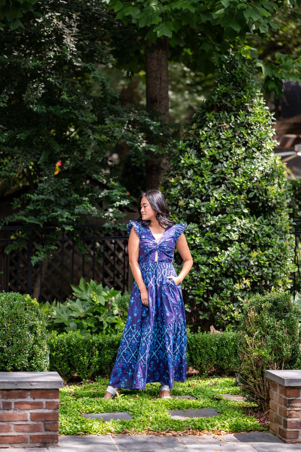Blue patterned maxi dress photographed in a lush garden setting with brick pillars.