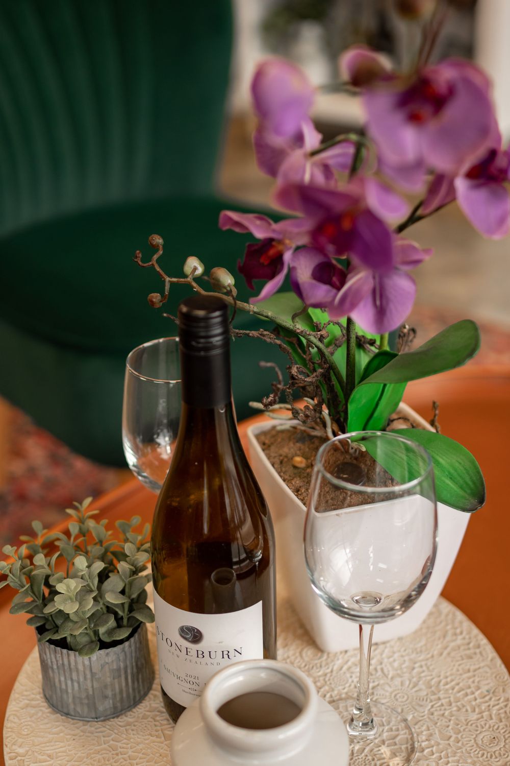 Wine bottle with orchid flower arrangement and empty wine glass on table.