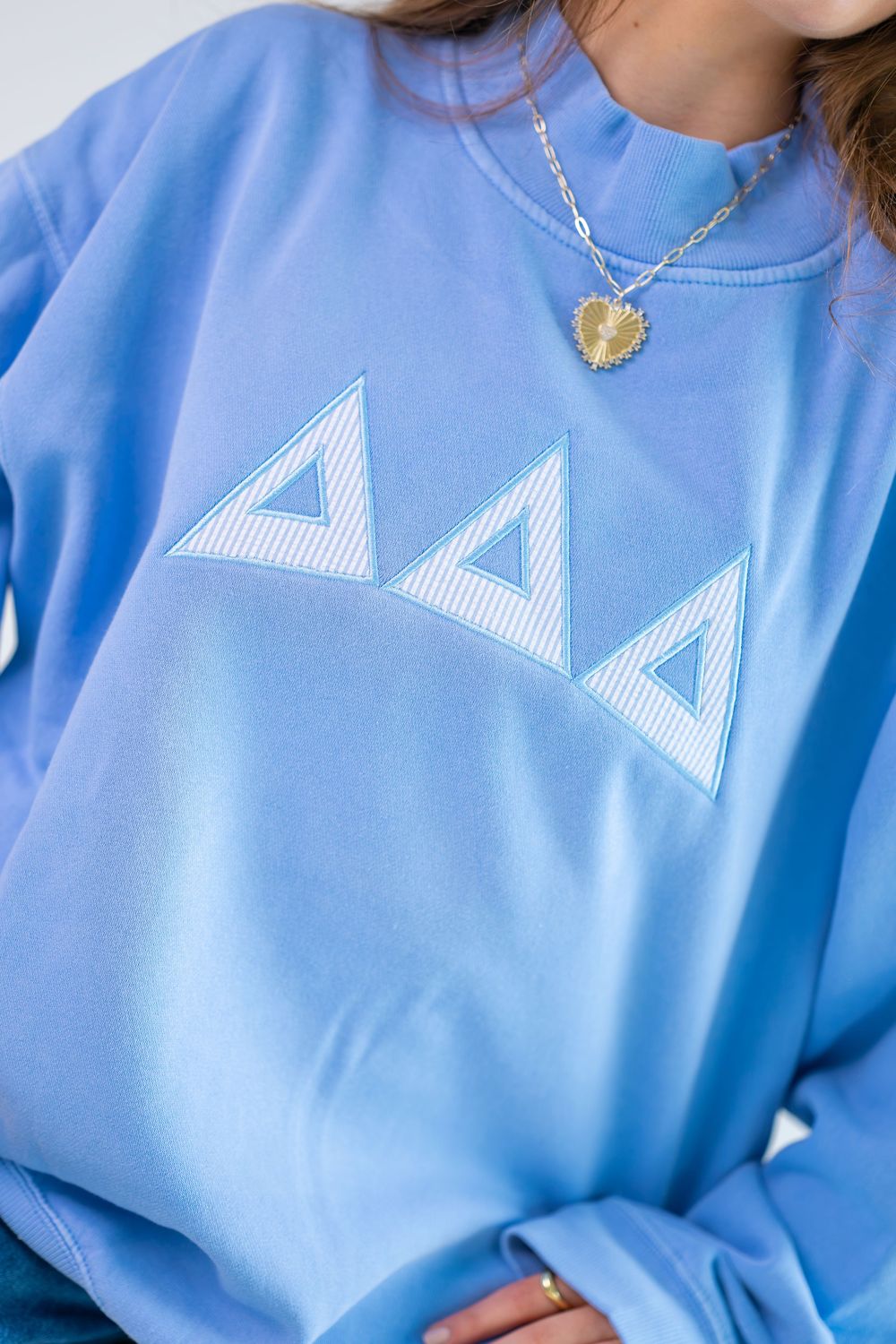 Light blue crewneck sweatshirt featuring embroidered Delta Delta Delta Greek letters in seersucker fabric pattern.