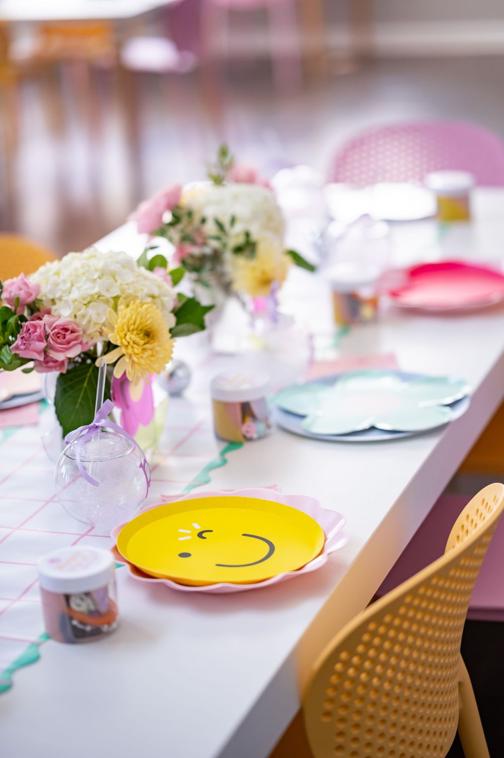 A cheerful party table setting with fresh flowers and a yellow smiley face plate.