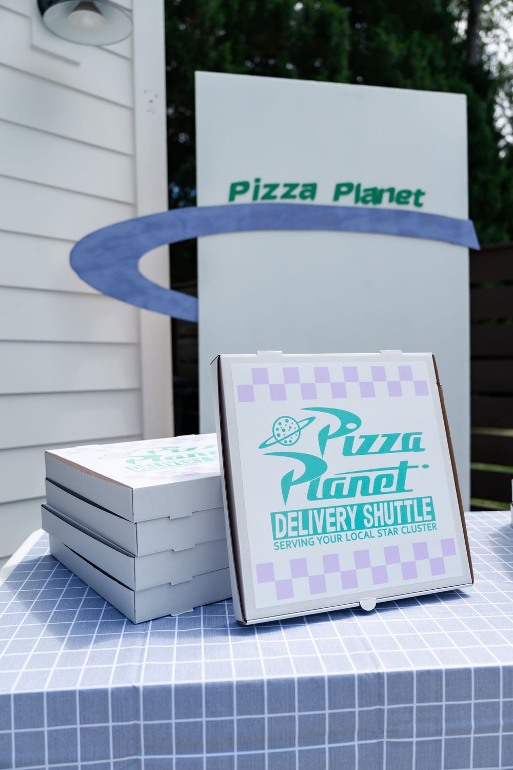Pizza Planet themed delivery boxes stacked on a table at a Toy Story inspired party with a Pizza Planet sign backdrop.