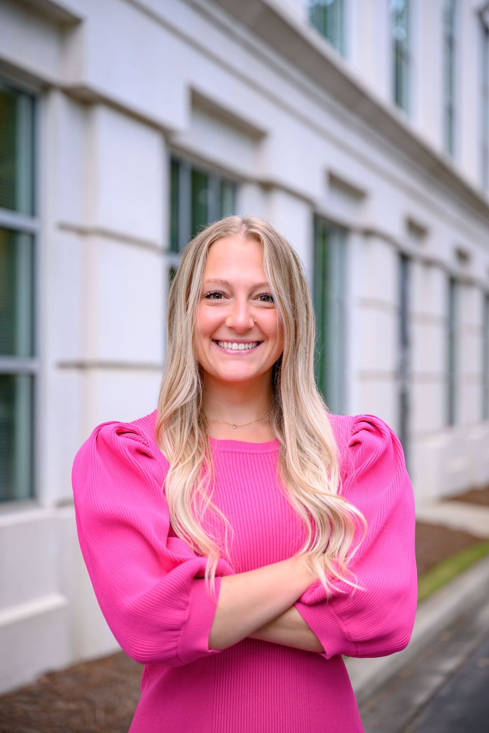 Woman in bright pink sweater with puff sleeves poses against white building exterior.