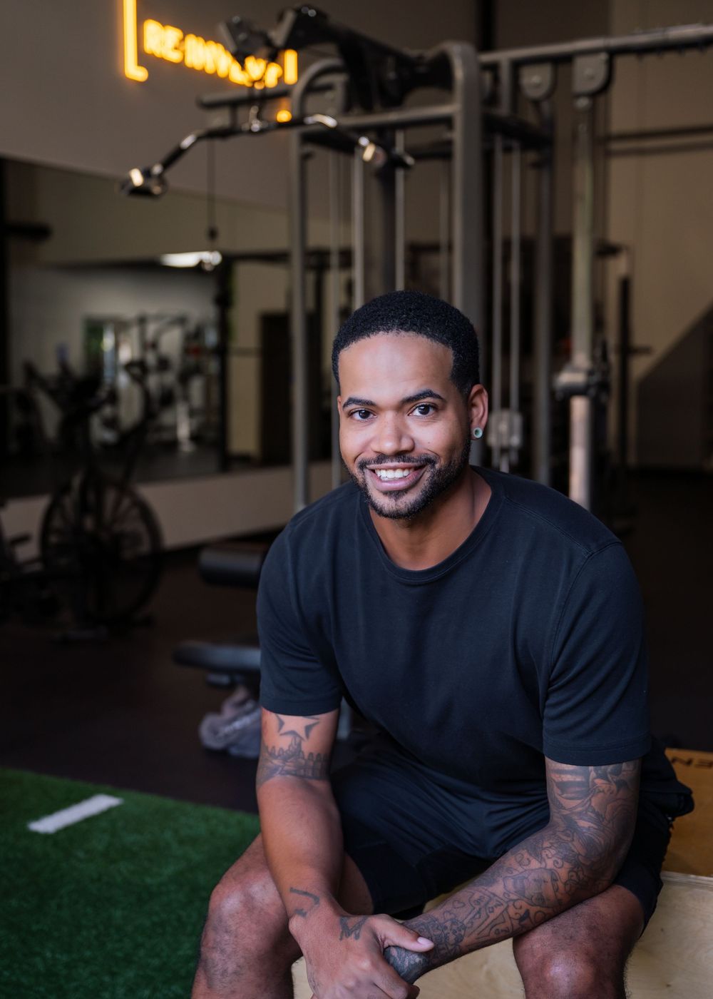 Athletic trainer in black t-shirt demonstrating exercises in a modern gym facility.