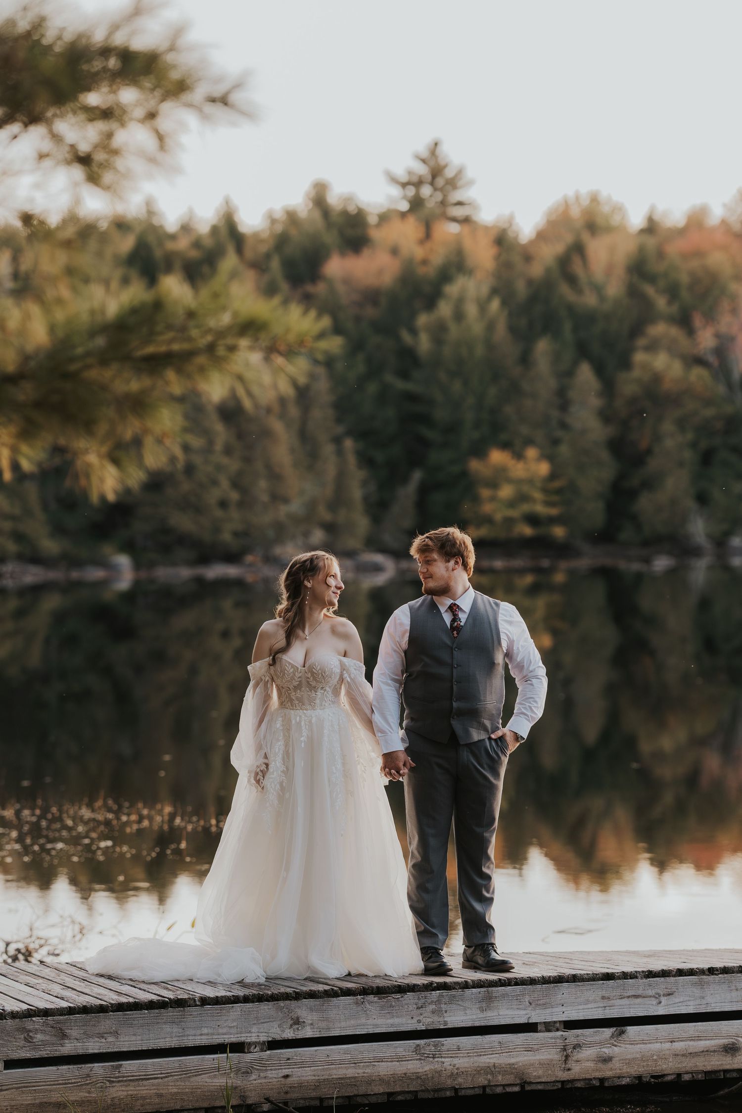 Wedding pair sitting on rustic bench with colorful decorations in field in New Hampshire.