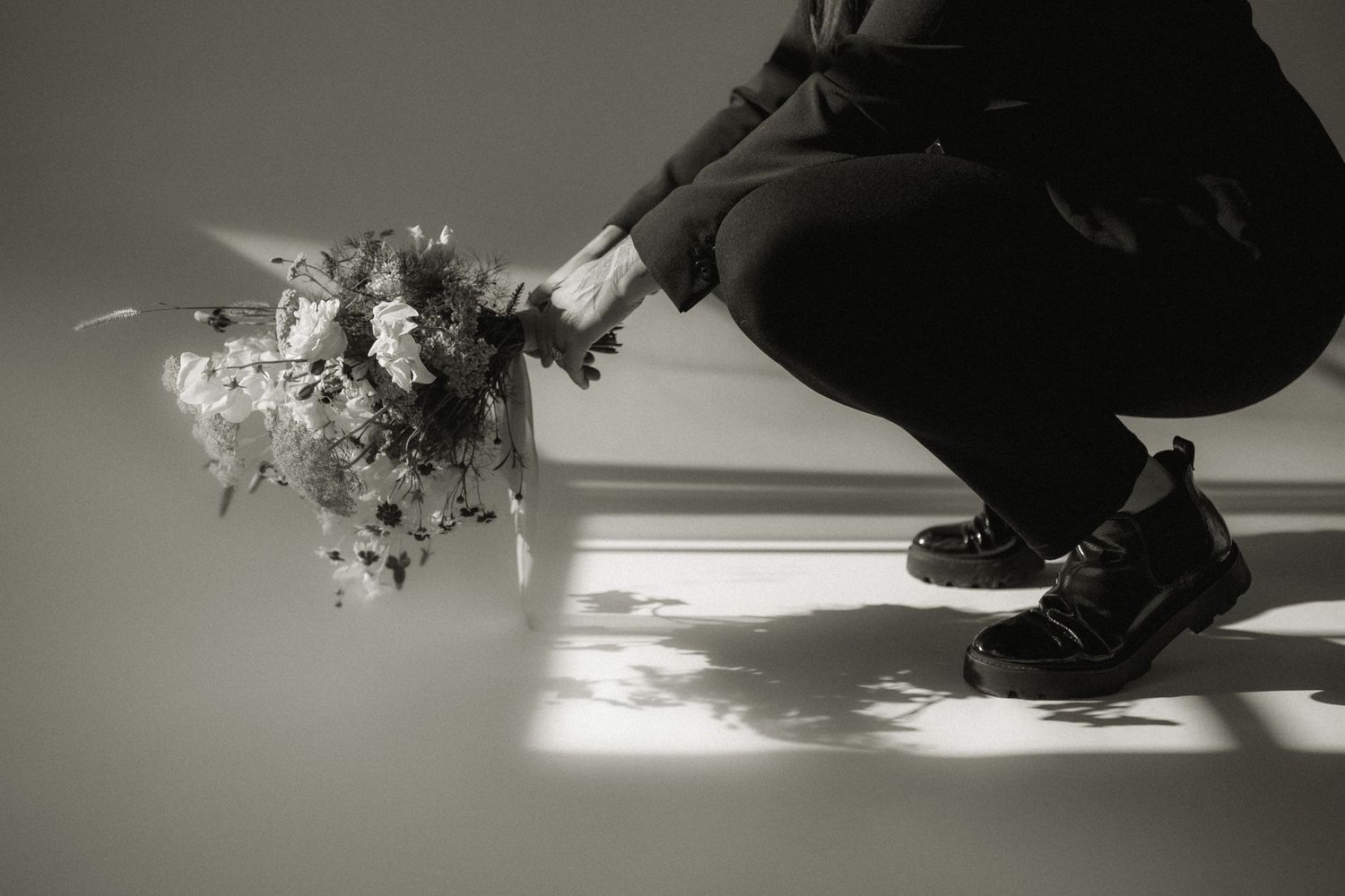 Dramatic black and white photo of someone holding a wildflower bouquet near the floor.