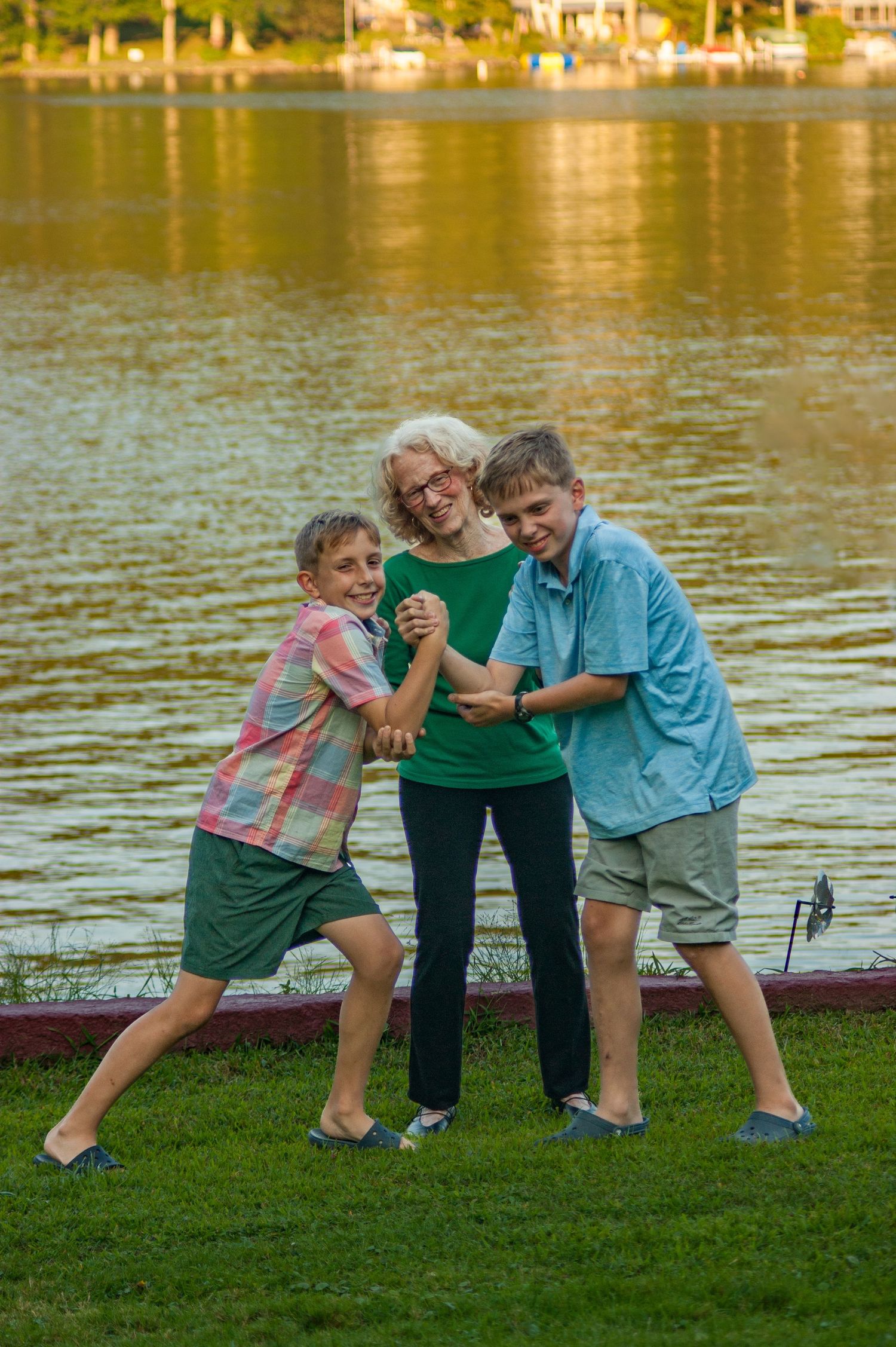 Three people playfully pose together on grass near a lake during sunset.