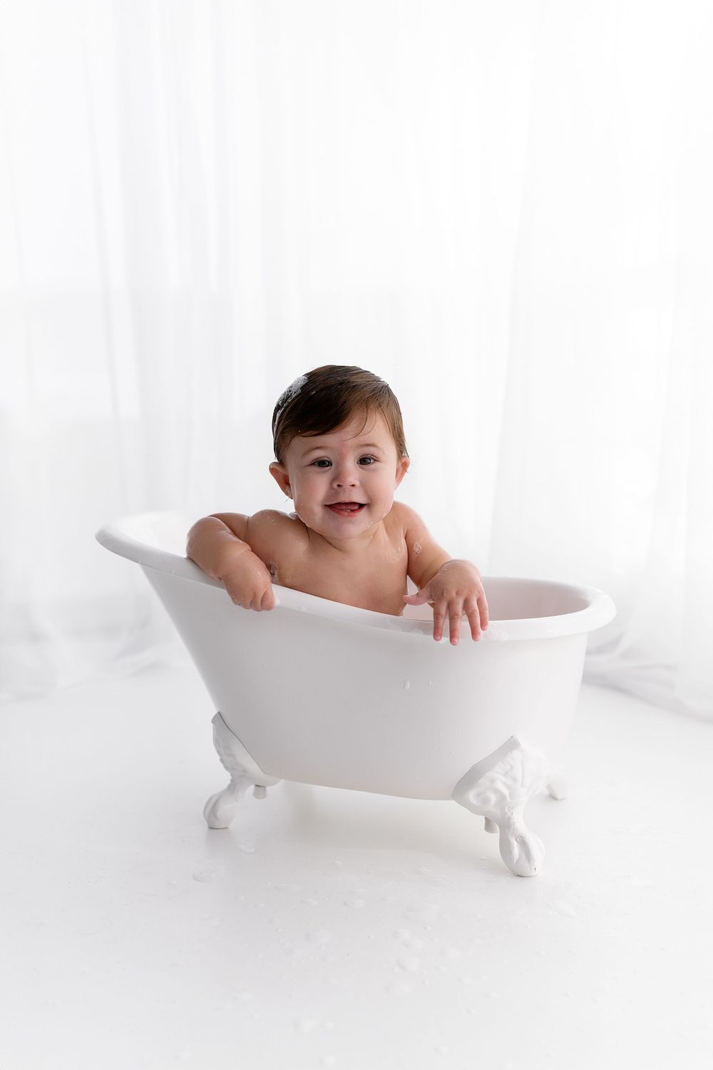 Baby sitting in decorative white clawfoot bathtub during studio photoshoot.