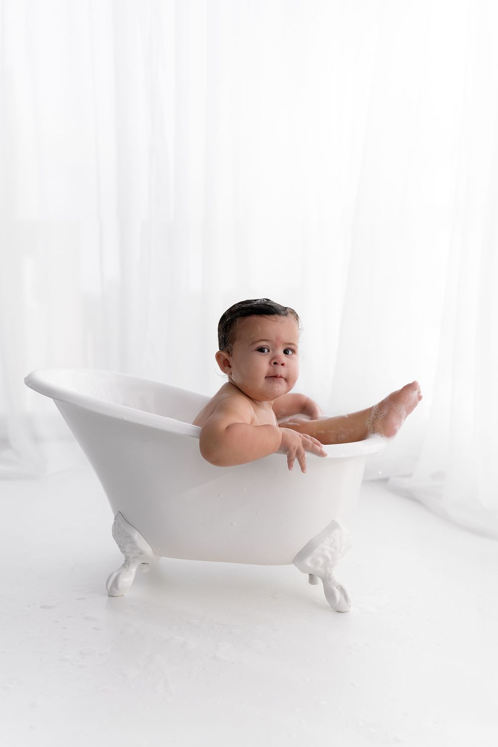 Baby playing in vintage white bathtub during minimalist studio photoshoot.