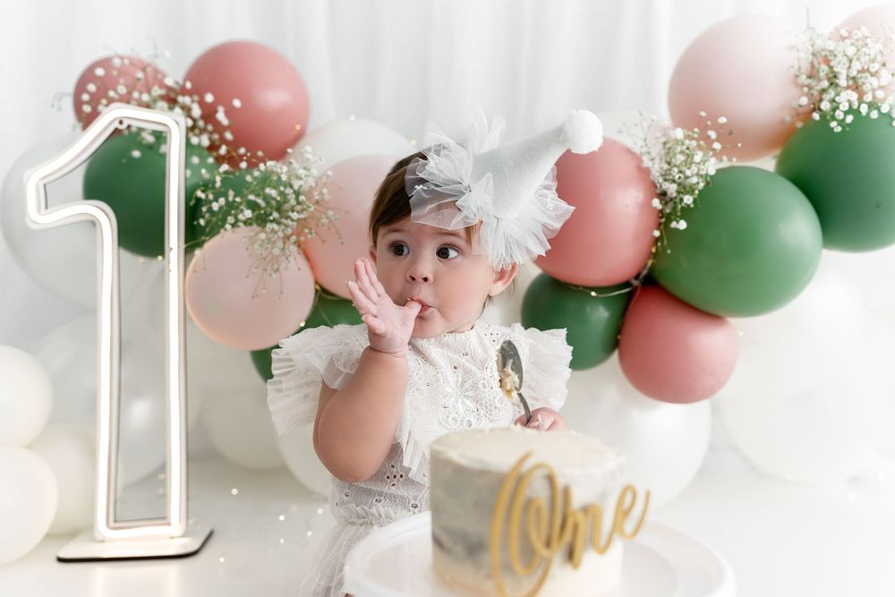 First birthday celebration with green and pink balloon garland and gold cake topper.