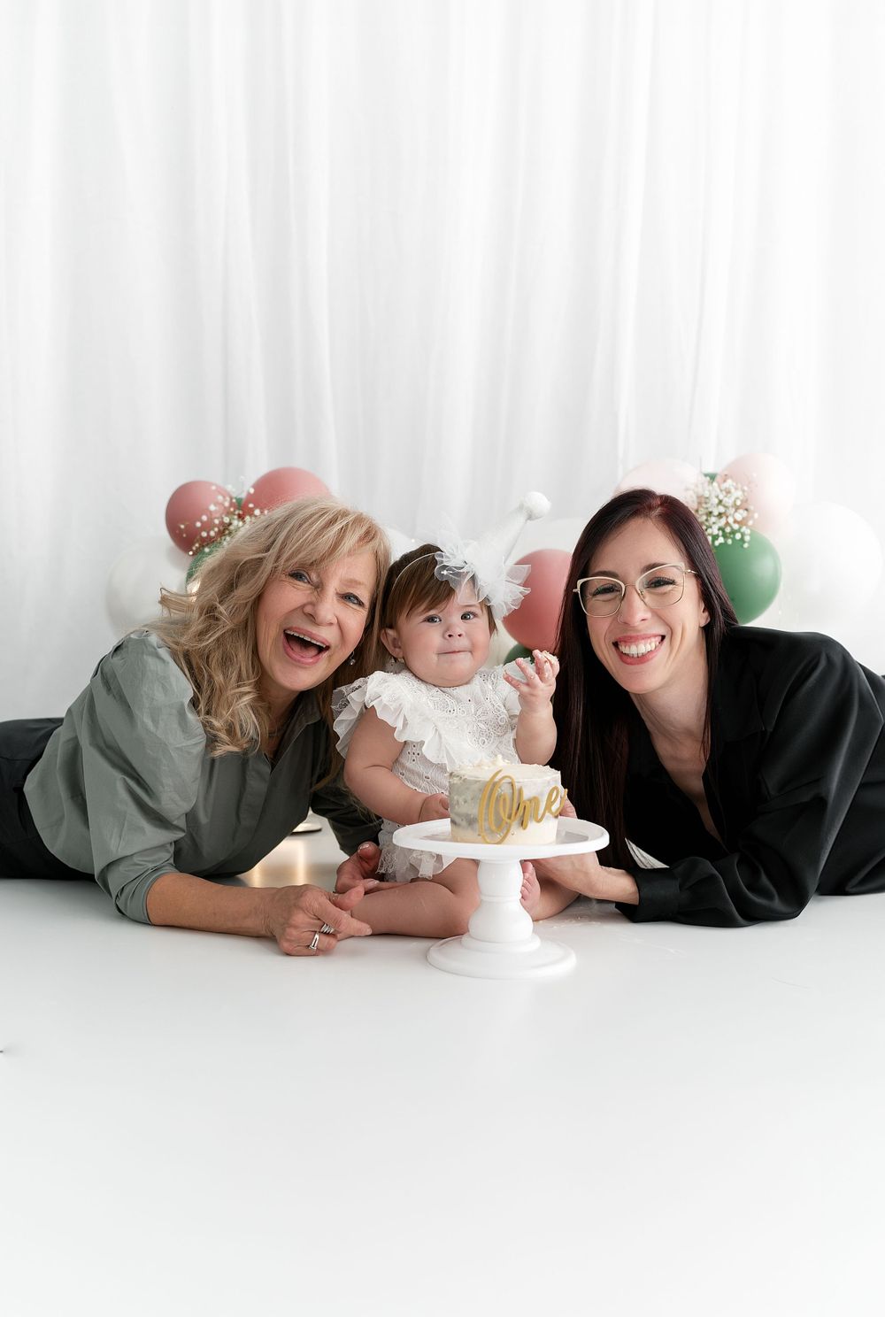 Family portrait with cake and festive balloon arch backdrop for first birthday celebration.