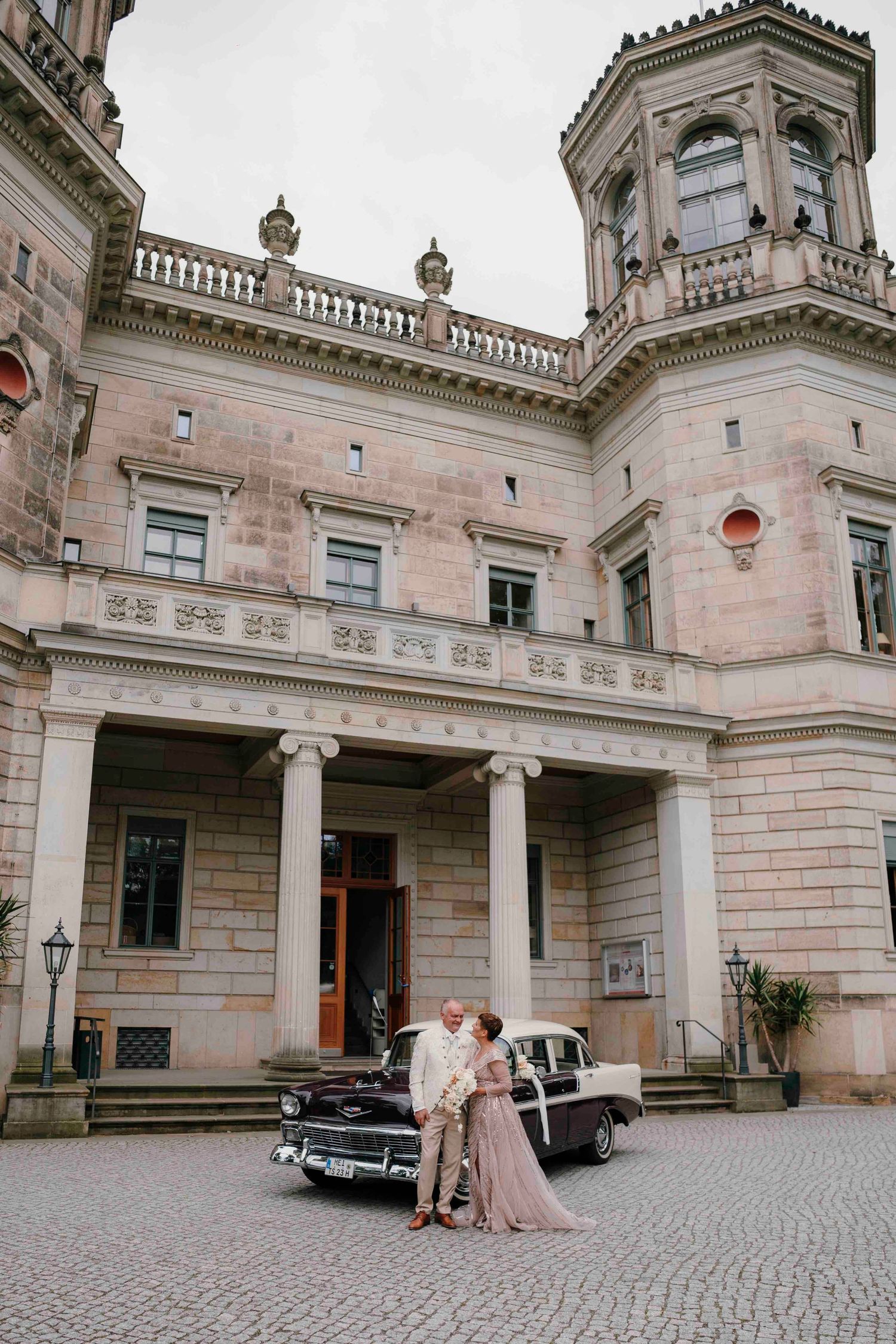 Classic vintage car parked in front of elegant stone palace with ornate architectural details.