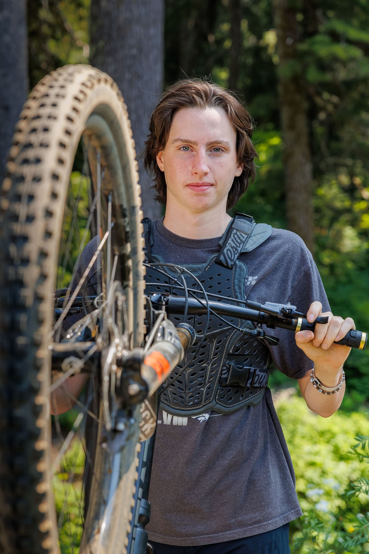 Mountain biker holds bike against a forest backdrop.