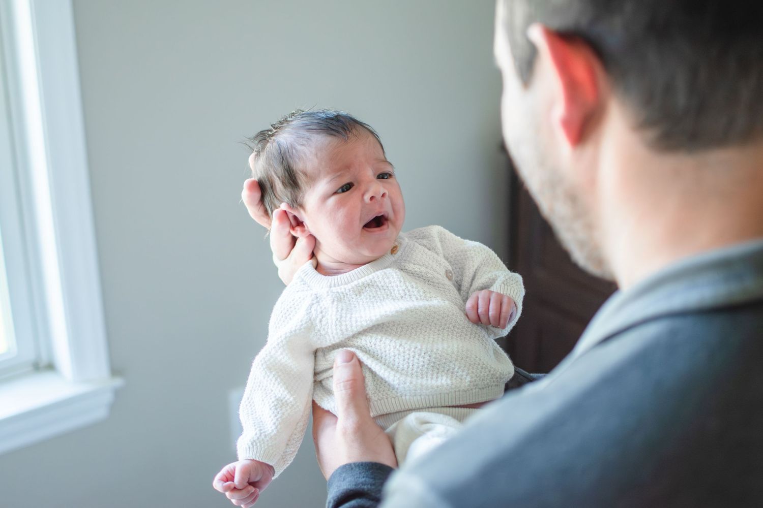 Baby girl looks at her dad as he holds her in the comfort of their home.