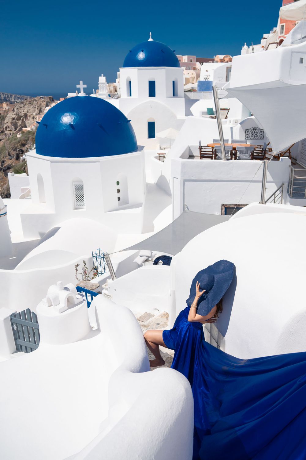 Blue-domed churches and white buildings of Santorini with flowing blue fabric in foreground.