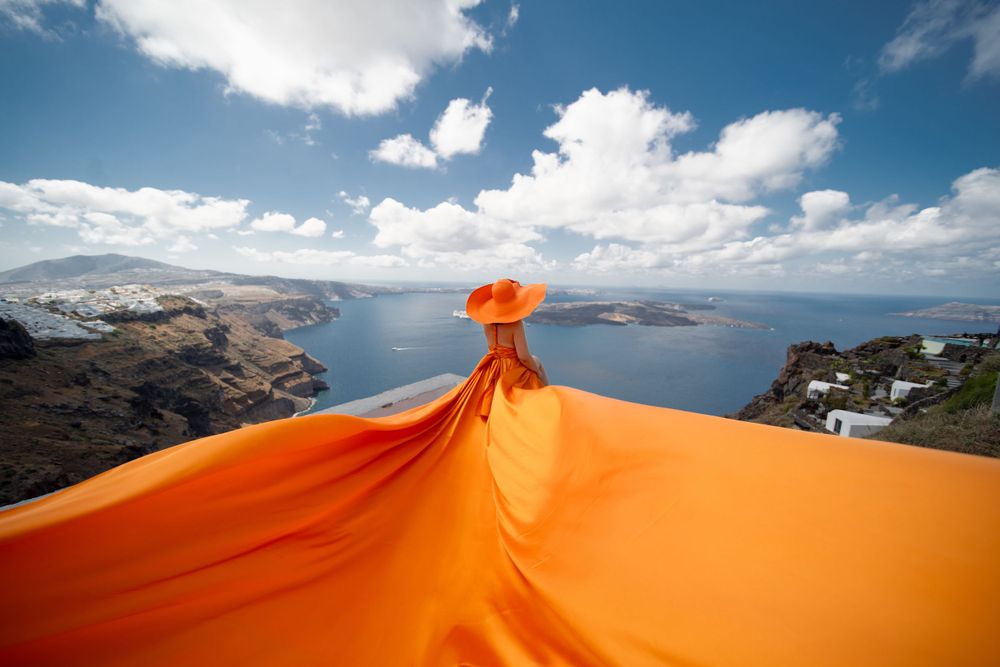 Flowing orange fabric billowing against Santorini's coastal landscape and blue sky.