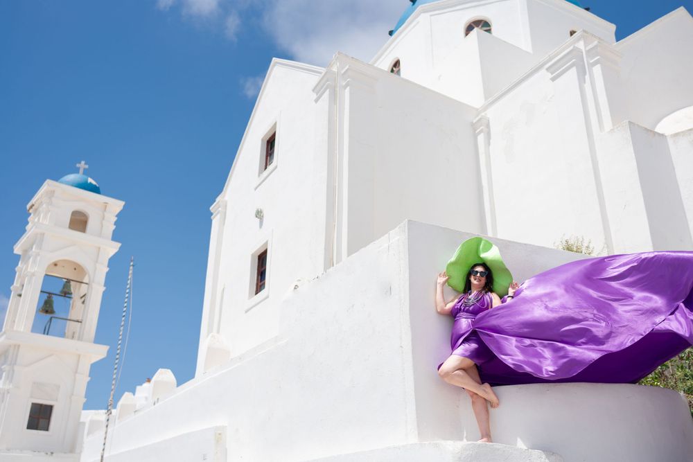 White church architecture in Santorini with flowing purple fabric against bright blue sky.