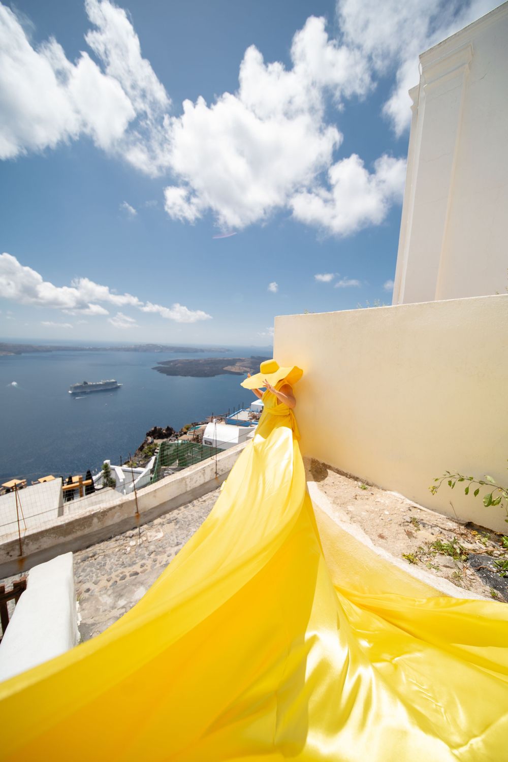 Yellow flowing fabric against white buildings overlooking the Aegean Sea and cruise ship in Santorini.
