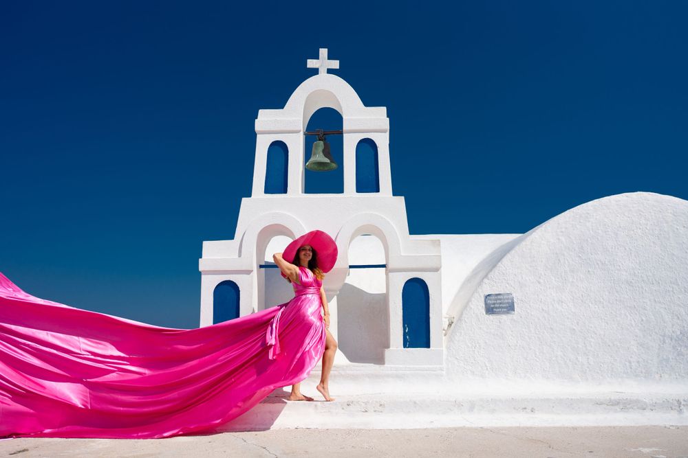 Pink flowing fabric against white church bell tower in Santorini, Greece.
