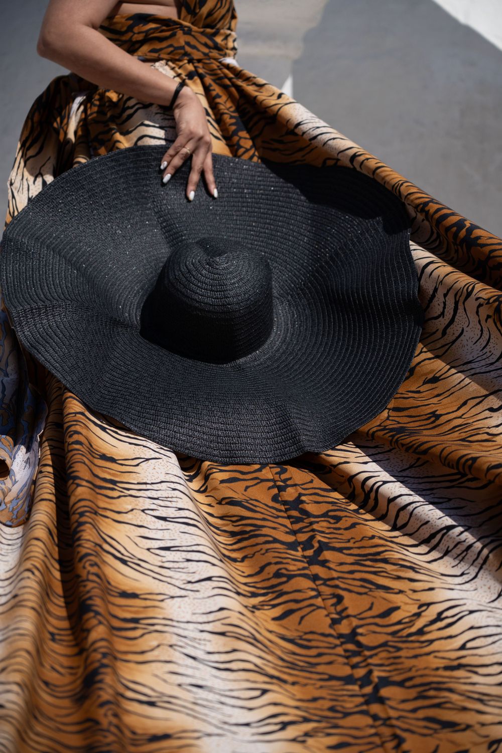 Large black sun hat on animal print fabric with dramatic lighting.